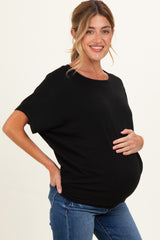 woman wearing a black maternity top and holding her baby bump while smiling