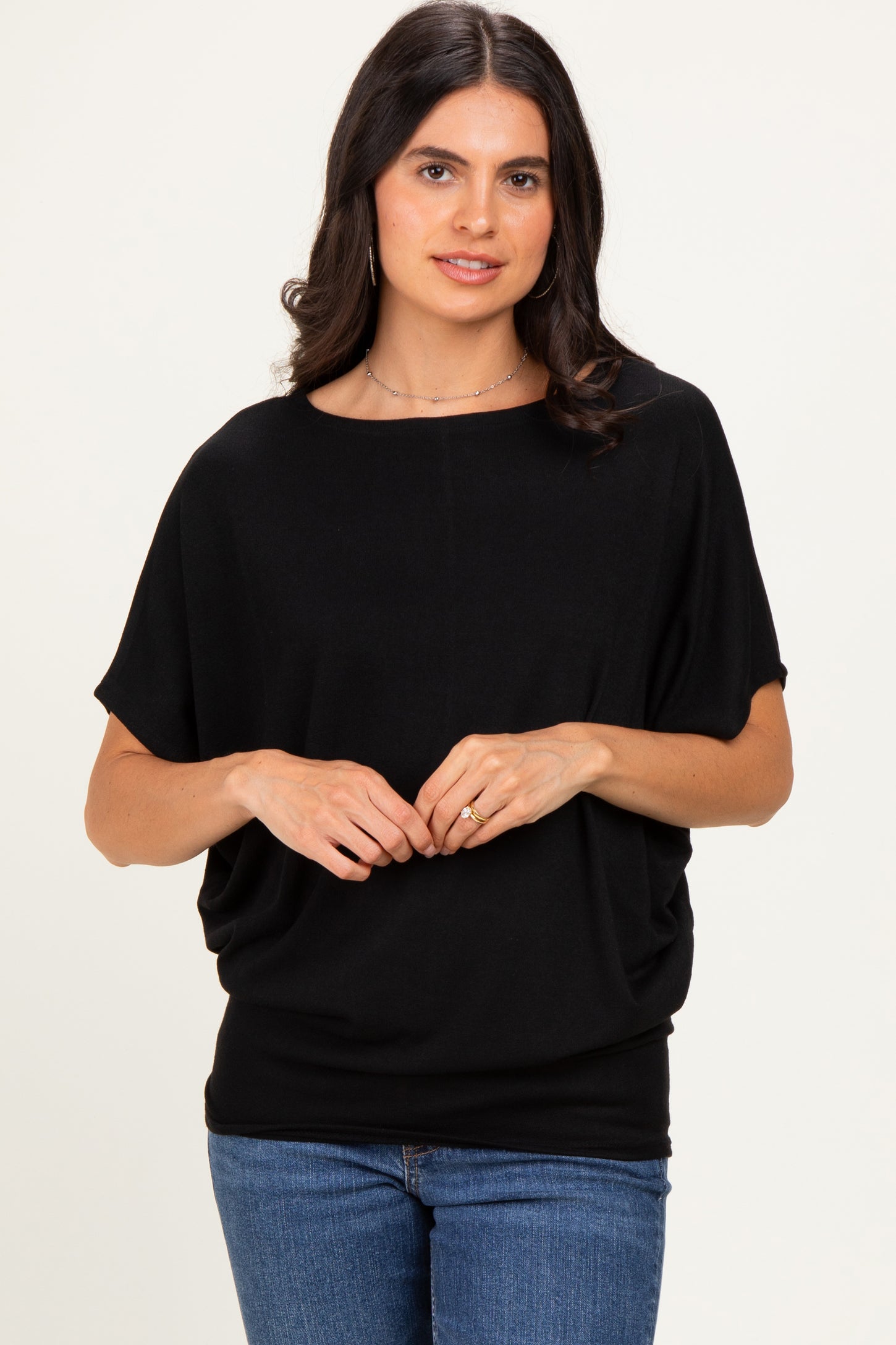 woman wearing a black draped short sleeve top with a round neckline and relaxed fit, paired with blue jeans