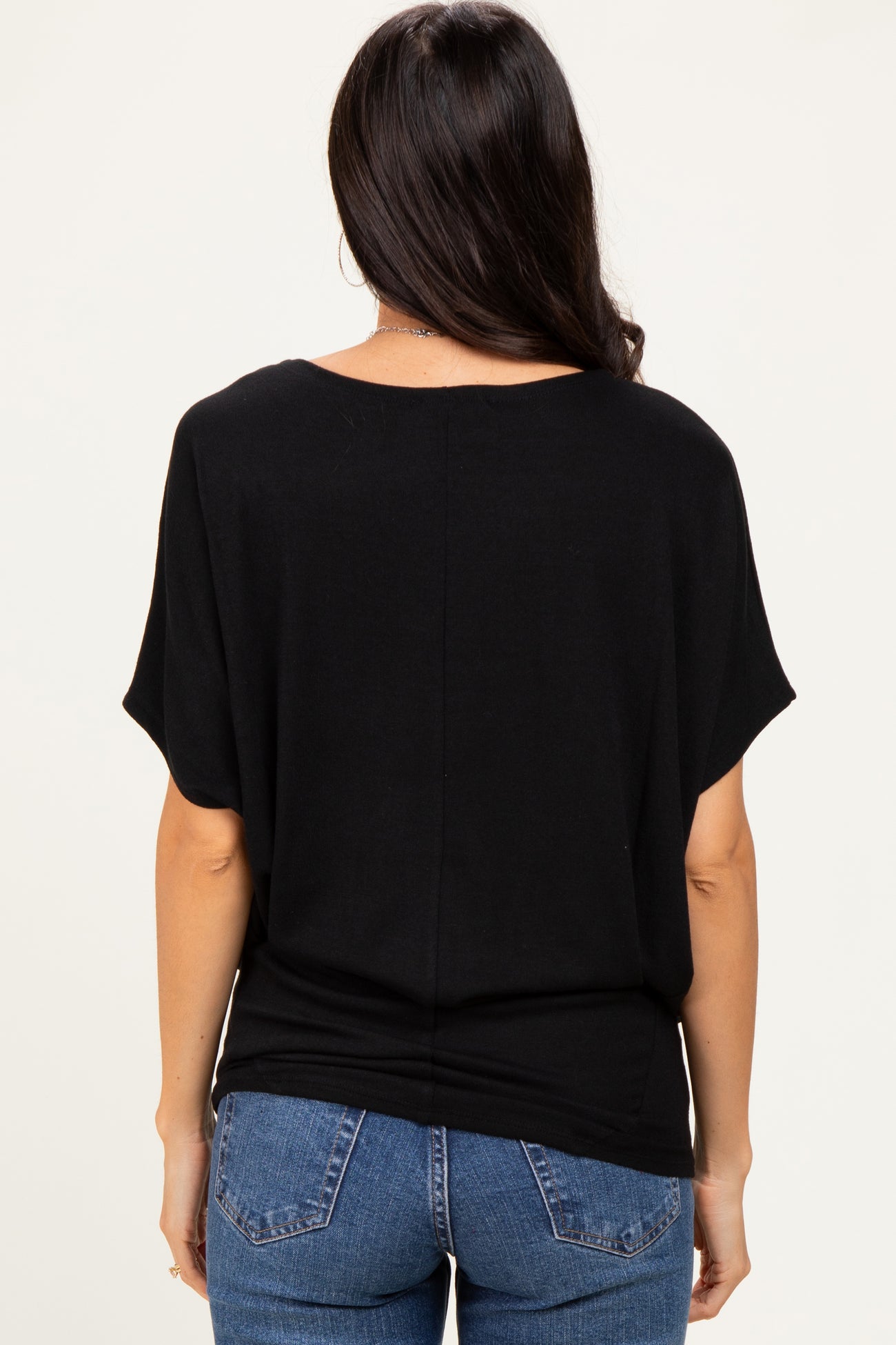 woman wearing a loose-fitting black top with short sleeves and back seam detail, paired with blue jeans