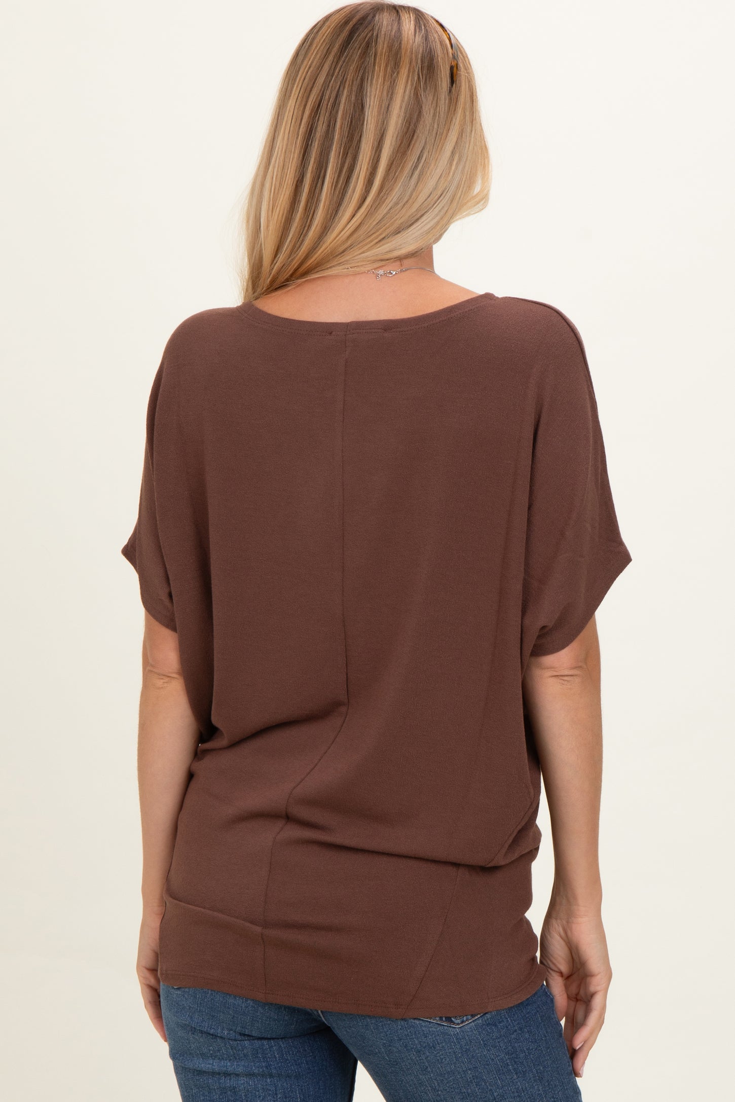 woman wearing a relaxed fit brown top with short sleeves, showing a simple back design and paired with blue jeans