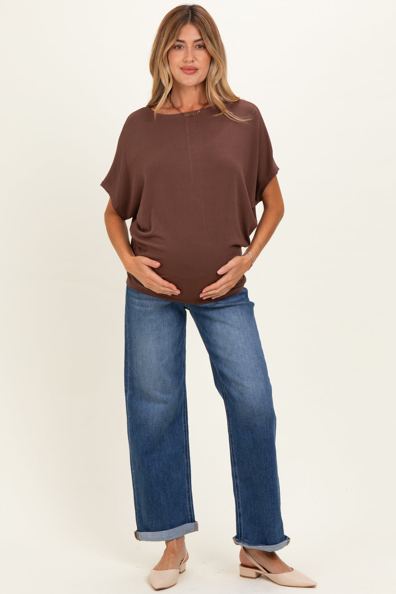 woman wearing a brown loose-fitting maternity top and blue wide-leg jeans, displaying her baby bump