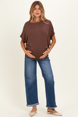 woman wearing a brown loose-fitting maternity top and blue wide-leg jeans, displaying her baby bump