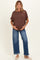 woman wearing a brown loose-fitting maternity top and blue wide-leg jeans, displaying her baby bump