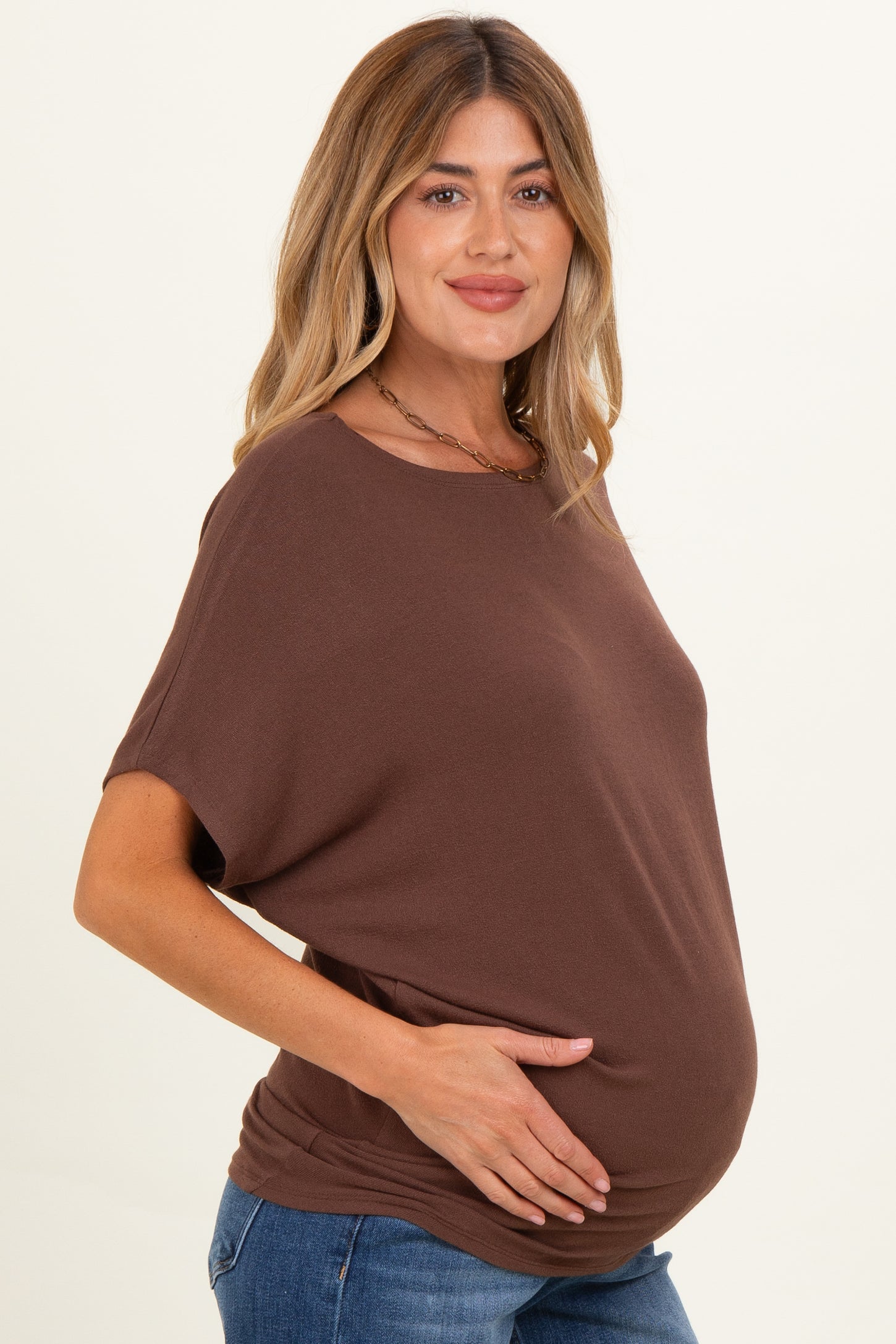 woman wearing a brown maternity top and holding her baby bump while smiling