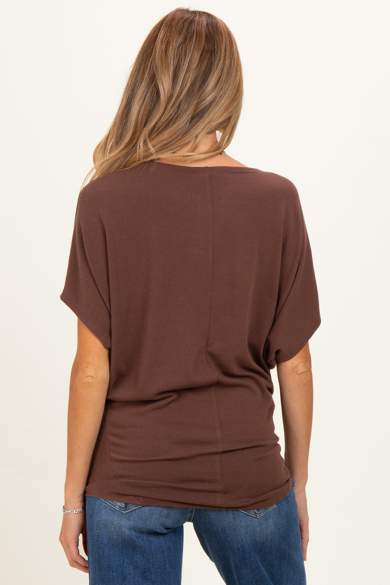 woman wearing a brown oversized maternity top and blue jeans, showing the back view of the top