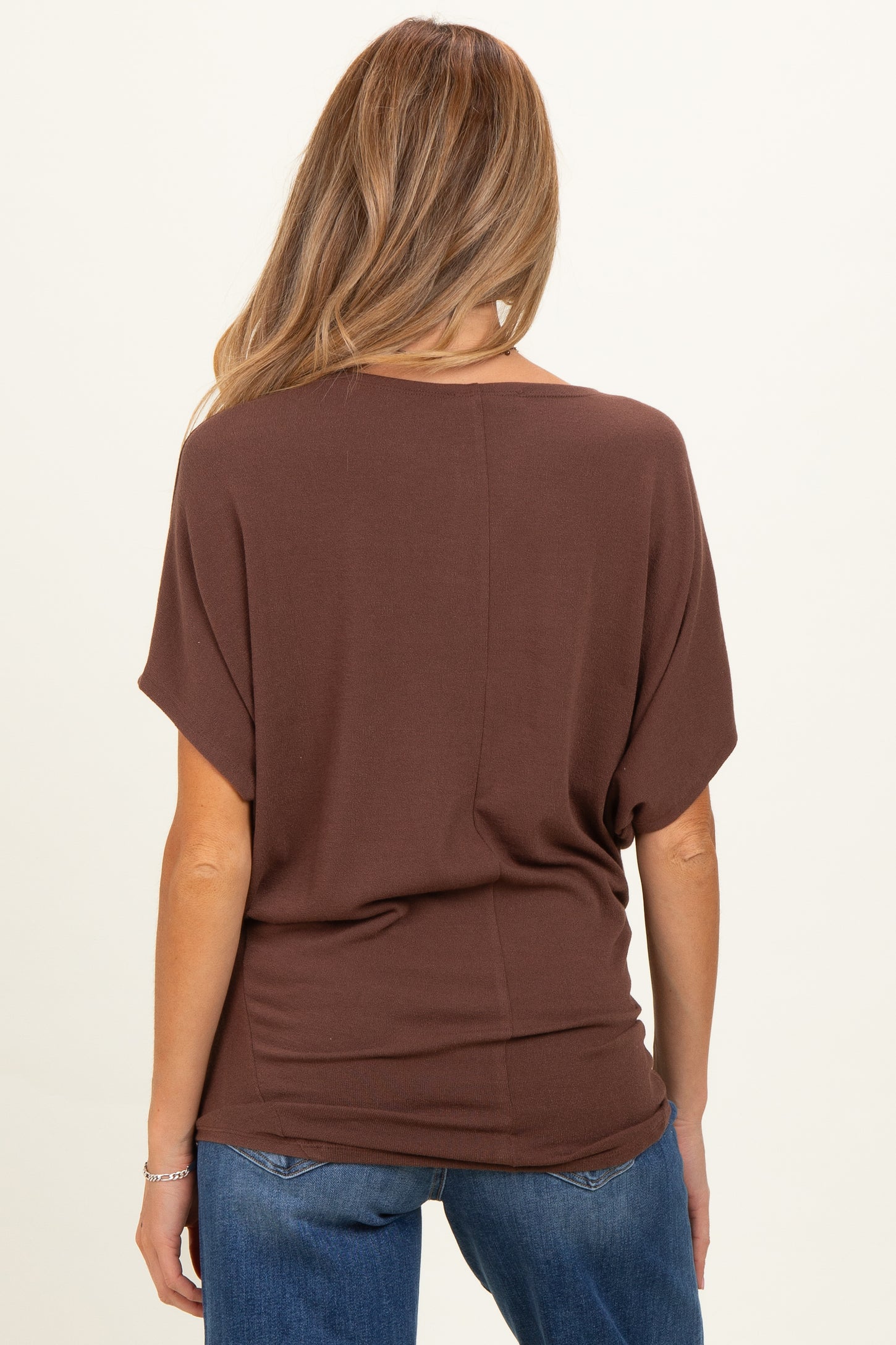 woman wearing a brown oversized maternity top and blue jeans, showing the back view of the top