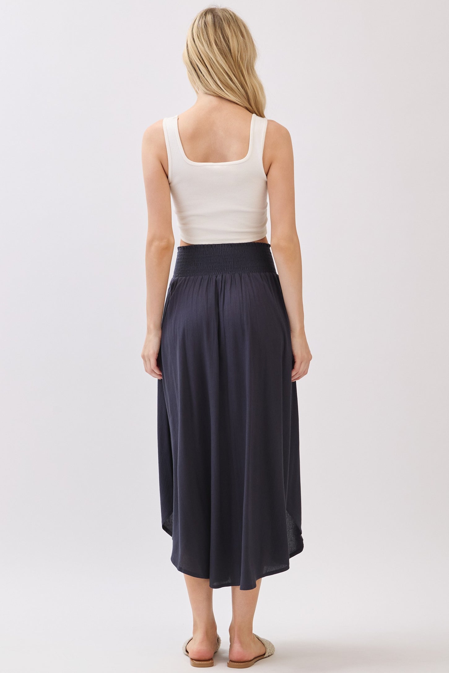 woman wearing a white tank top and a long, dark gray skirt, viewed from the back
