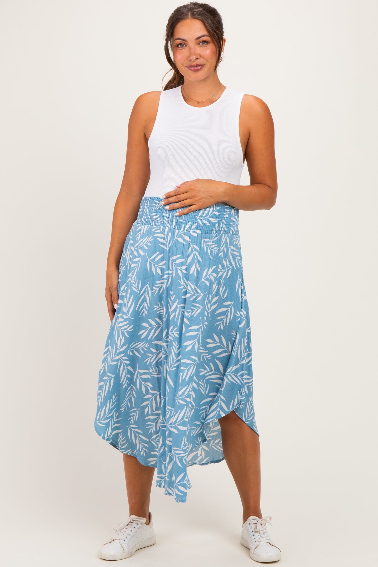 woman wearing a white sleeveless maternity top and a blue patterned maternity skirt, holding her baby bump