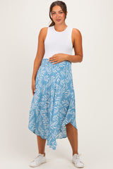 woman wearing a white sleeveless maternity top and a blue patterned maternity skirt, holding her baby bump