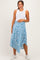 woman wearing a white sleeveless maternity top and a blue patterned maternity skirt, holding her baby bump