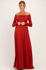 woman wearing a rust off-the-shoulder long sleeve maternity dress, gently holding her baby bump