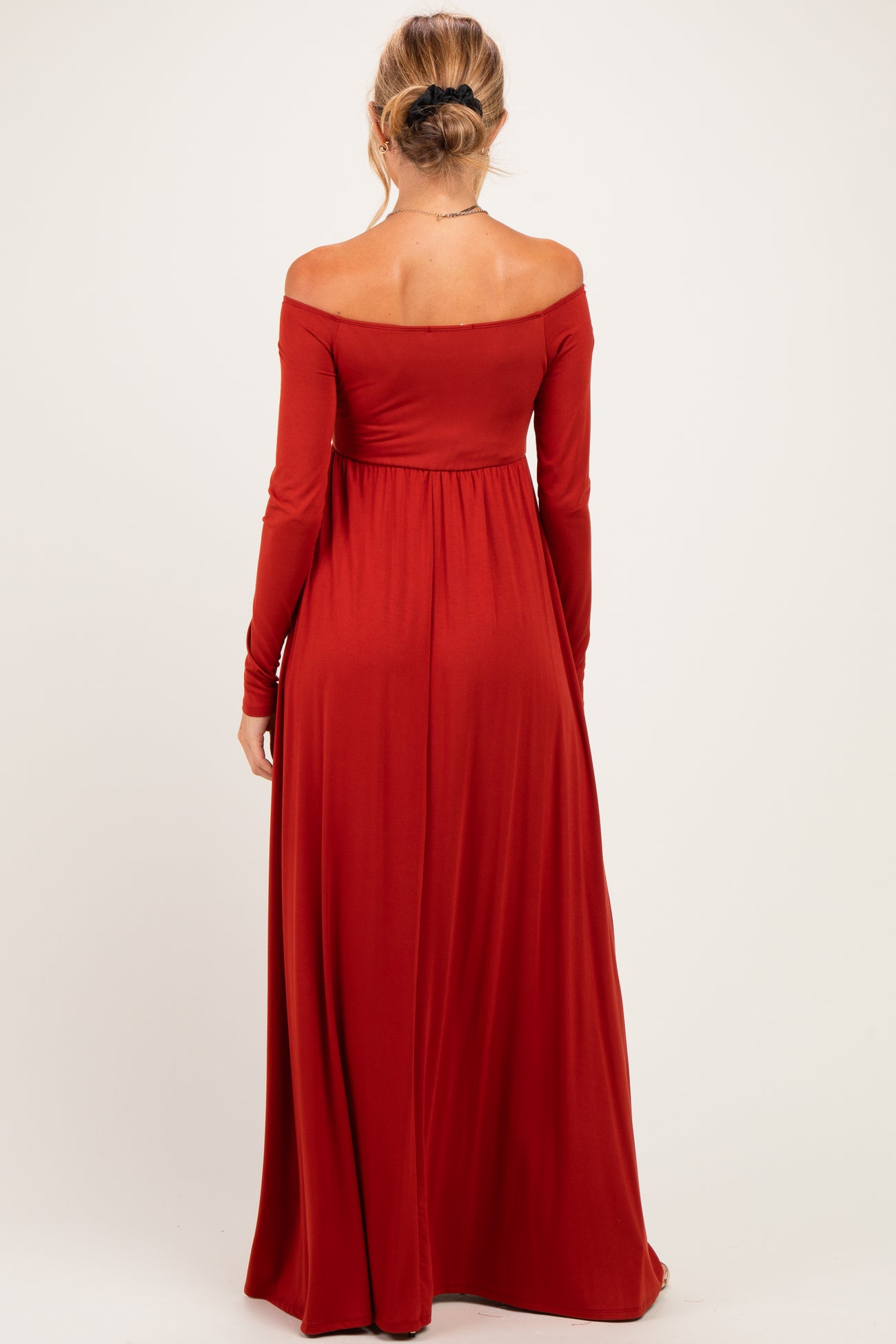 woman wearing a red off-the-shoulder maternity dress with long sleeves and a flowing skirt, showing a baby bump