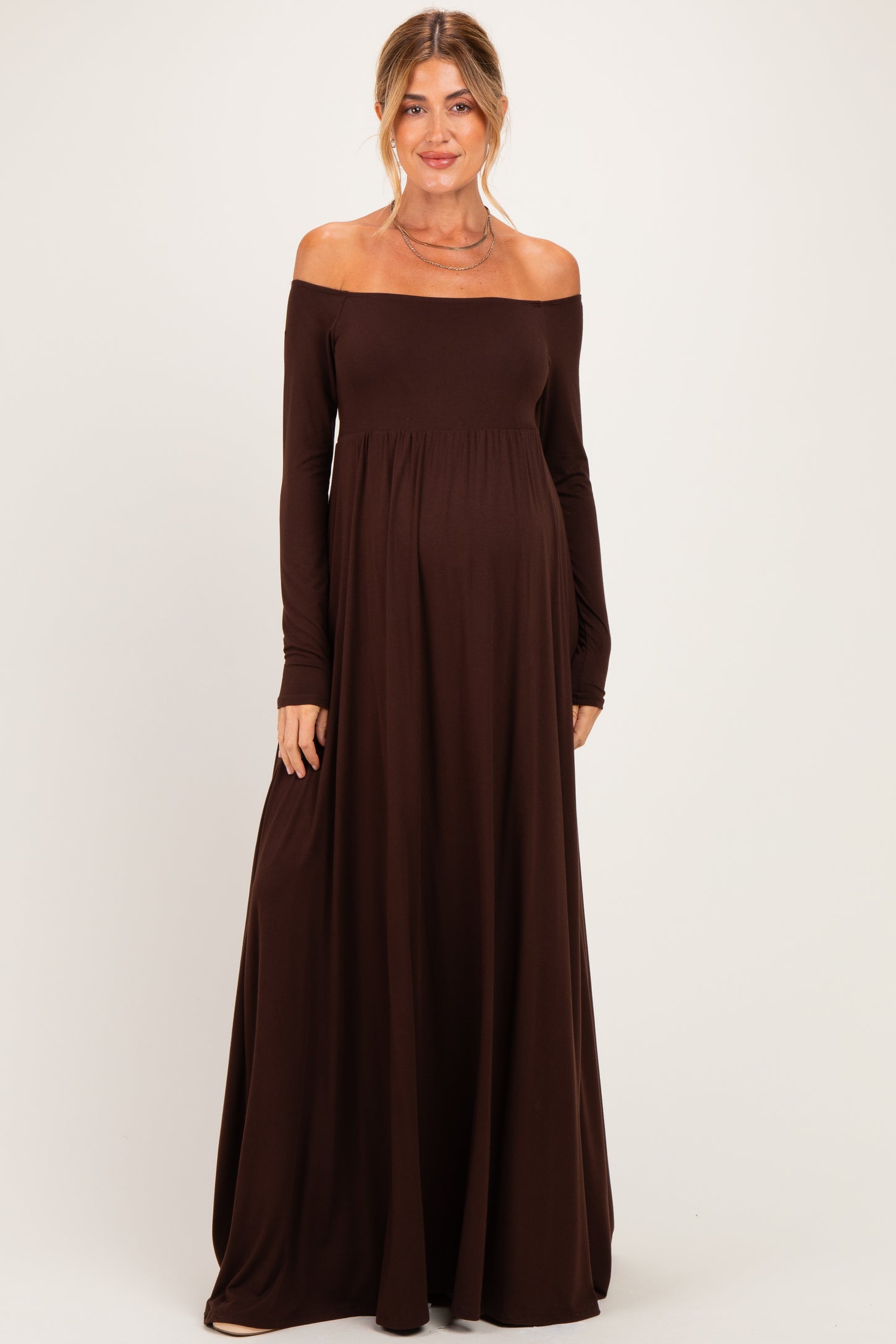 woman wearing a brown off-the-shoulder long sleeve maternity dress with a flowing skirt and visible baby bump