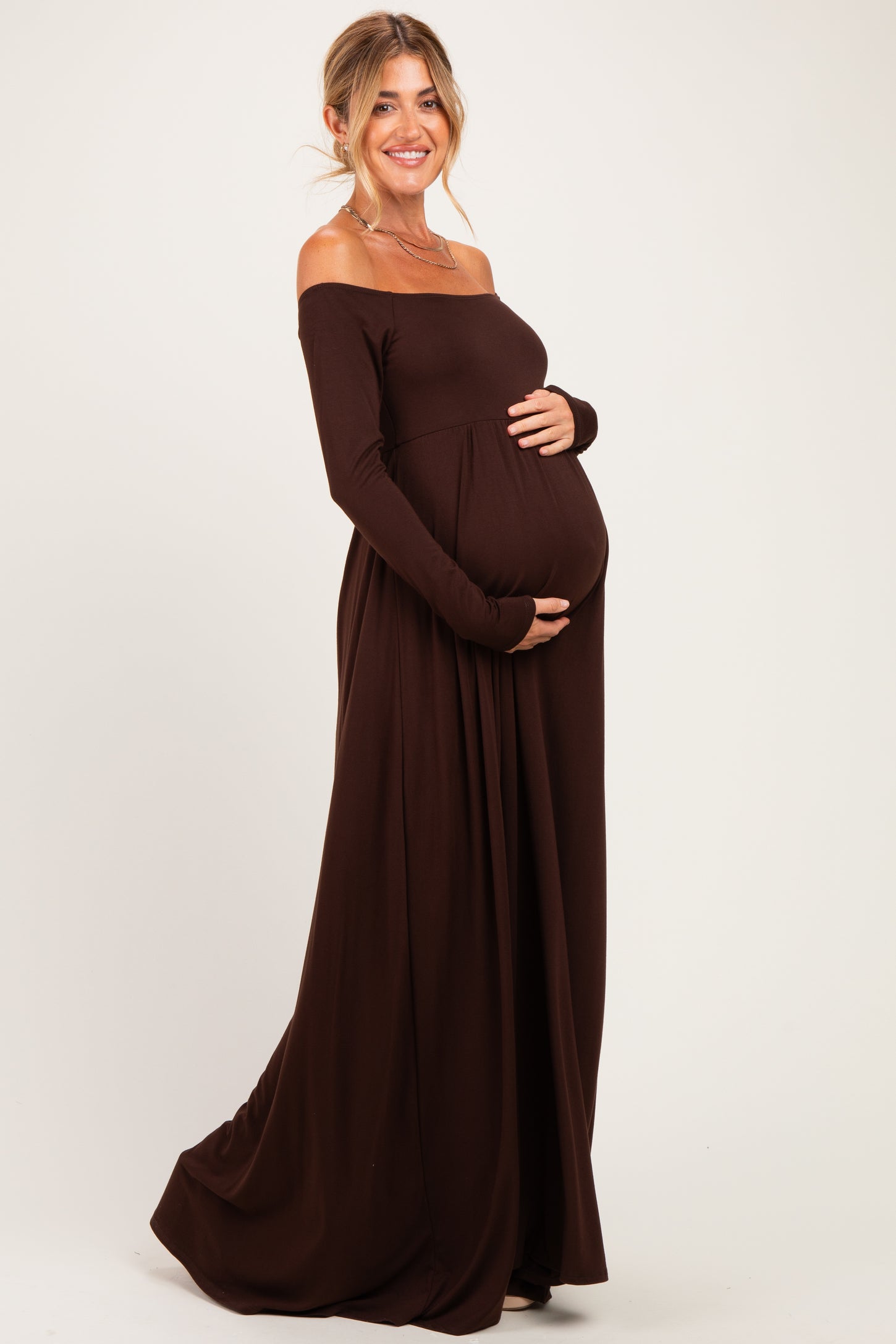 woman wearing a brown off-the-shoulder maternity maxi dress and holding her baby bump