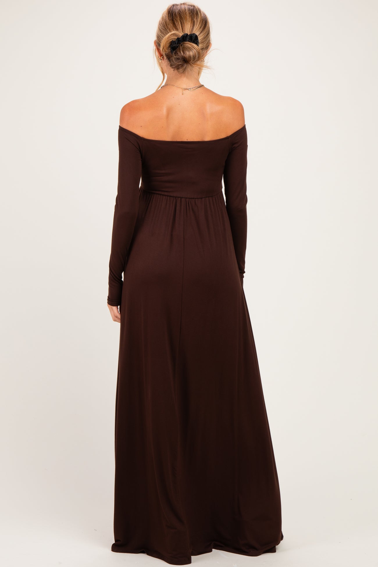 woman wearing a chocolate brown off-the-shoulder maternity maxi dress, showing a flowing silhouette from behind