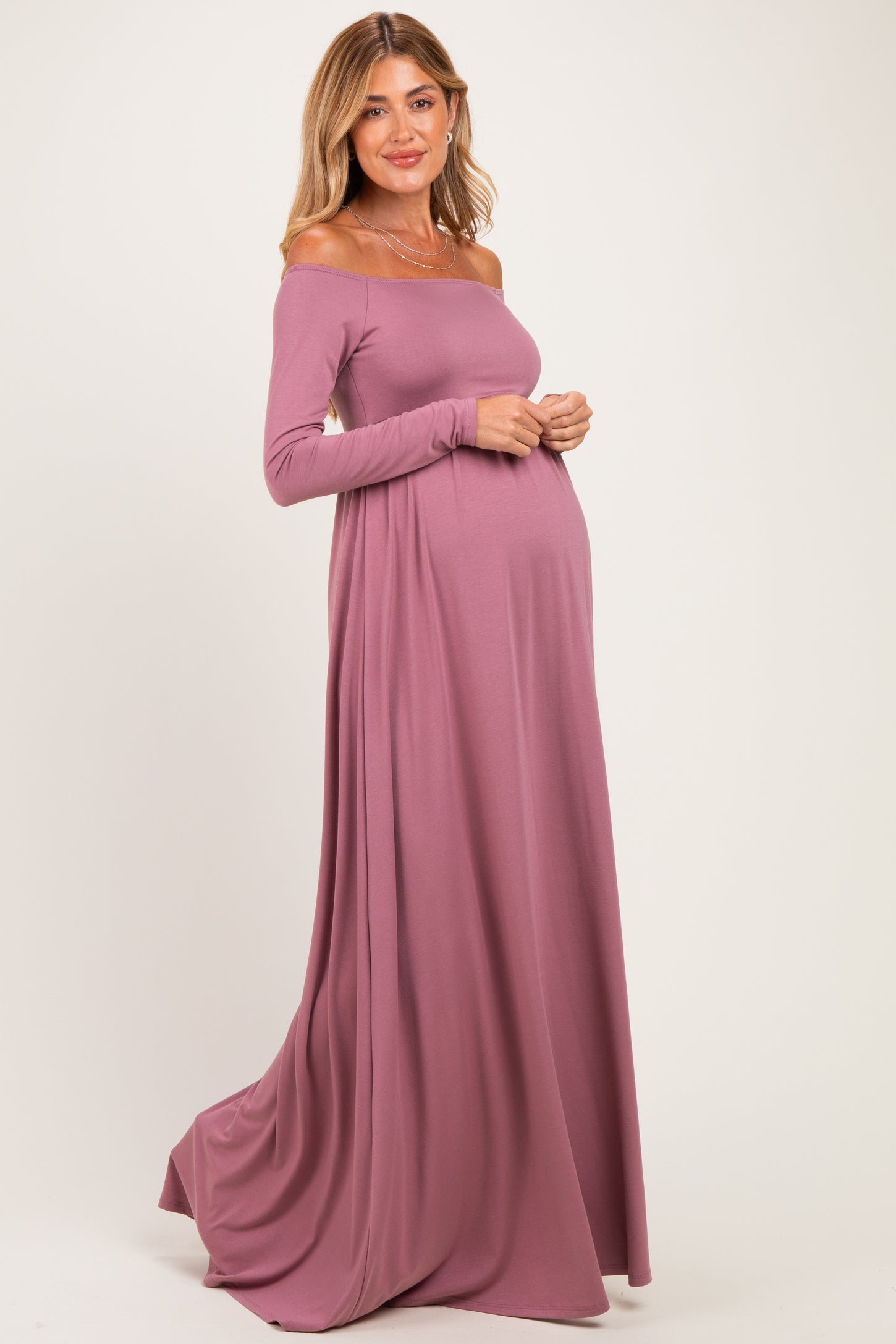 woman wearing a dusty rose off-the-shoulder maternity gown with long sleeves and a visible baby bump