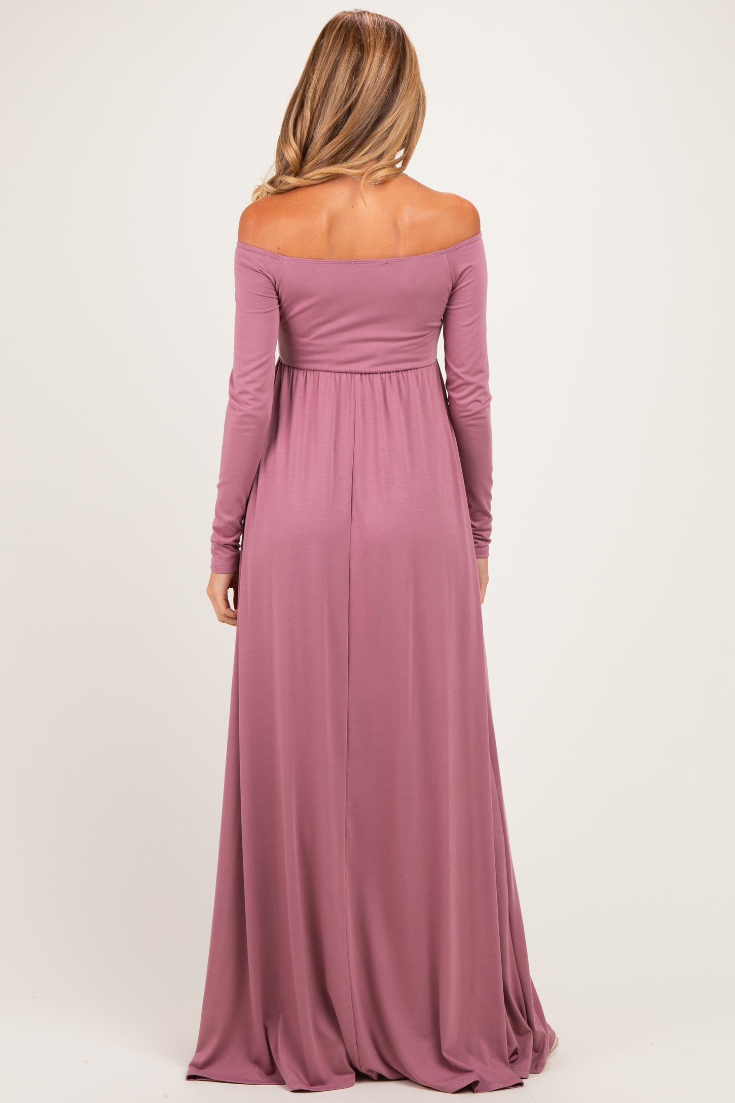 woman wearing a mauve off-the-shoulder maternity maxi dress with long sleeves and flowy skirt, showing a baby bump from the back