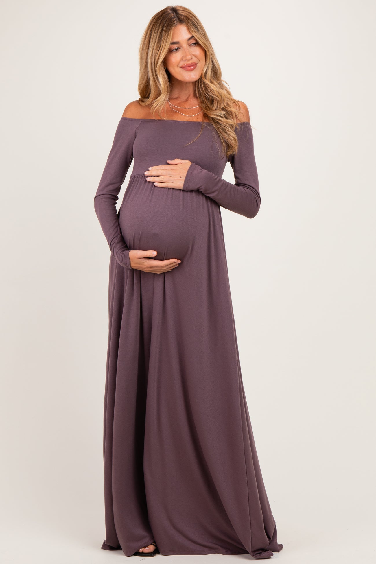 woman wearing a mauve off-the-shoulder maternity gown and holding her baby bump