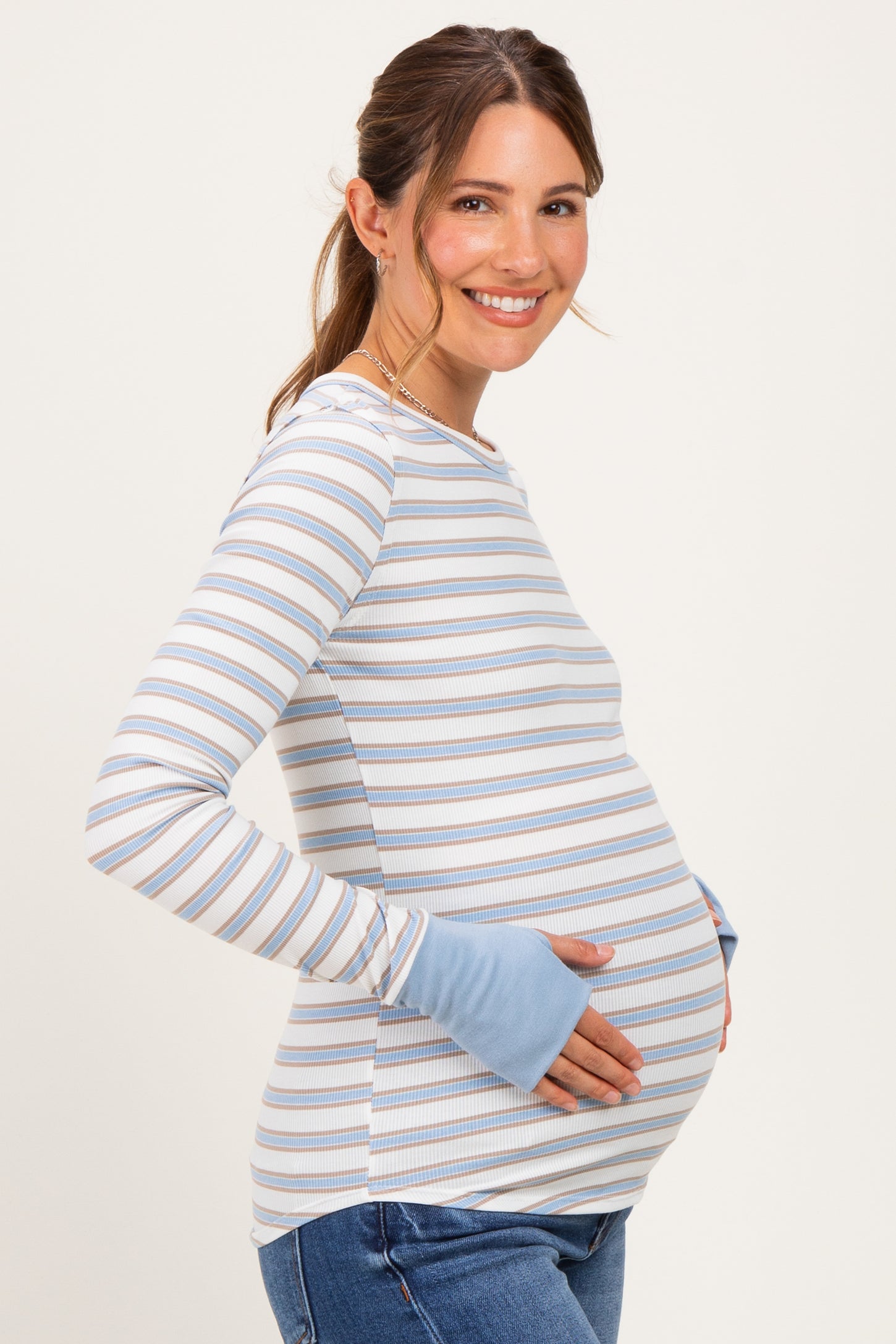 woman wearing a blue and white striped maternity top and holding her baby bump with a smile