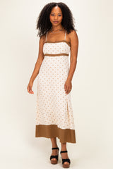woman wearing a cream polka dot maxi dress with adjustable straps and a brown hem, standing in a pose