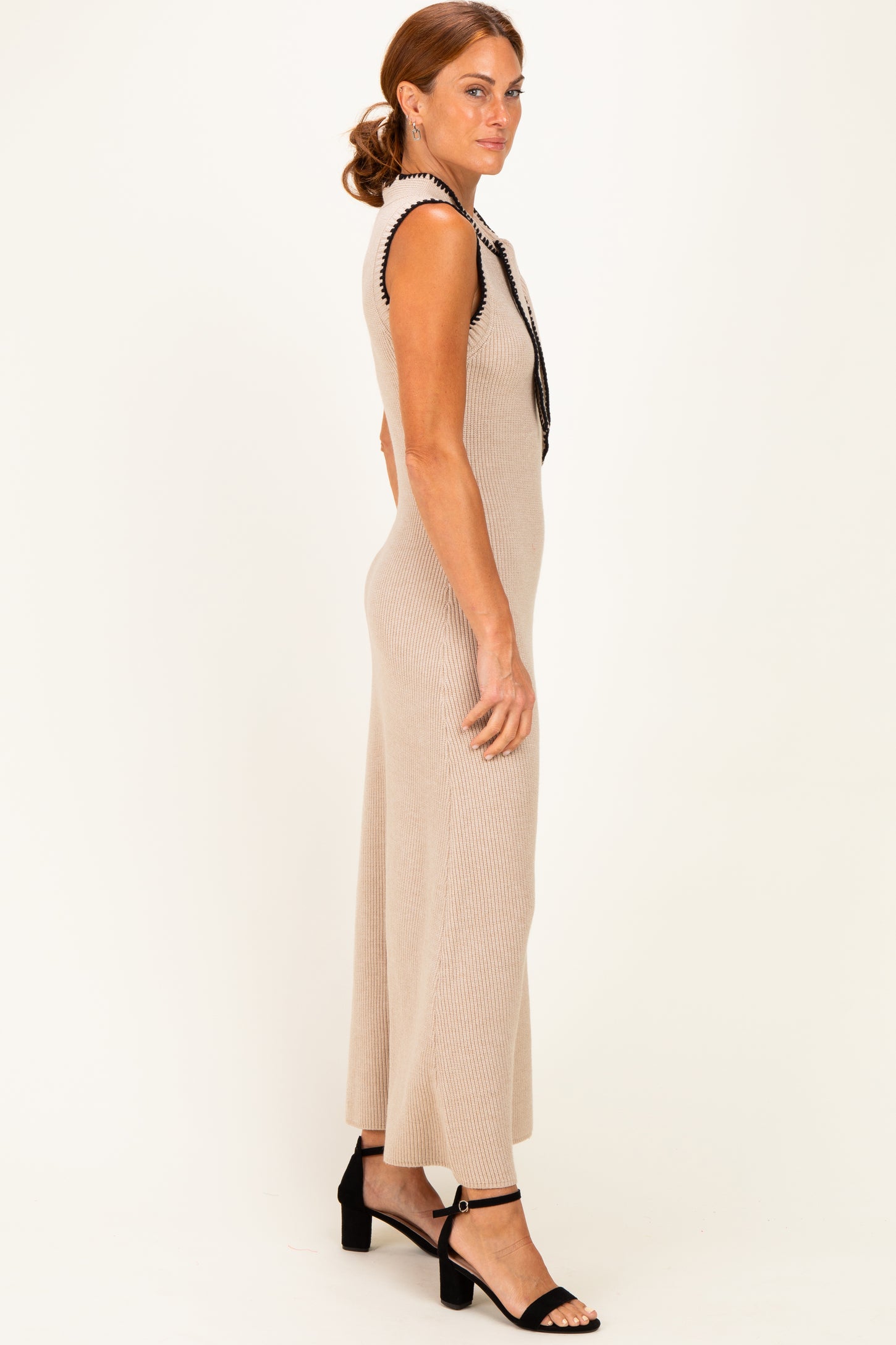 woman wearing a beige ribbed knit sleeveless dress with black trim and strappy black heels