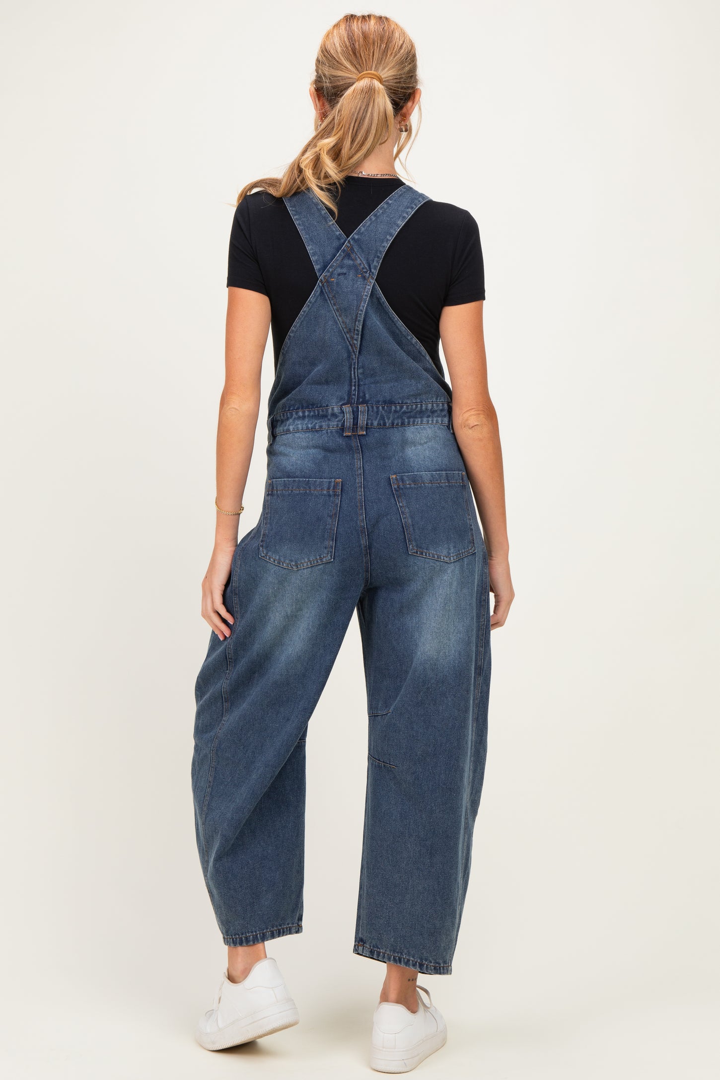 woman wearing a dark blue maternity denim overalls with a relaxed fit and pockets, styled with a black t-shirt underneath