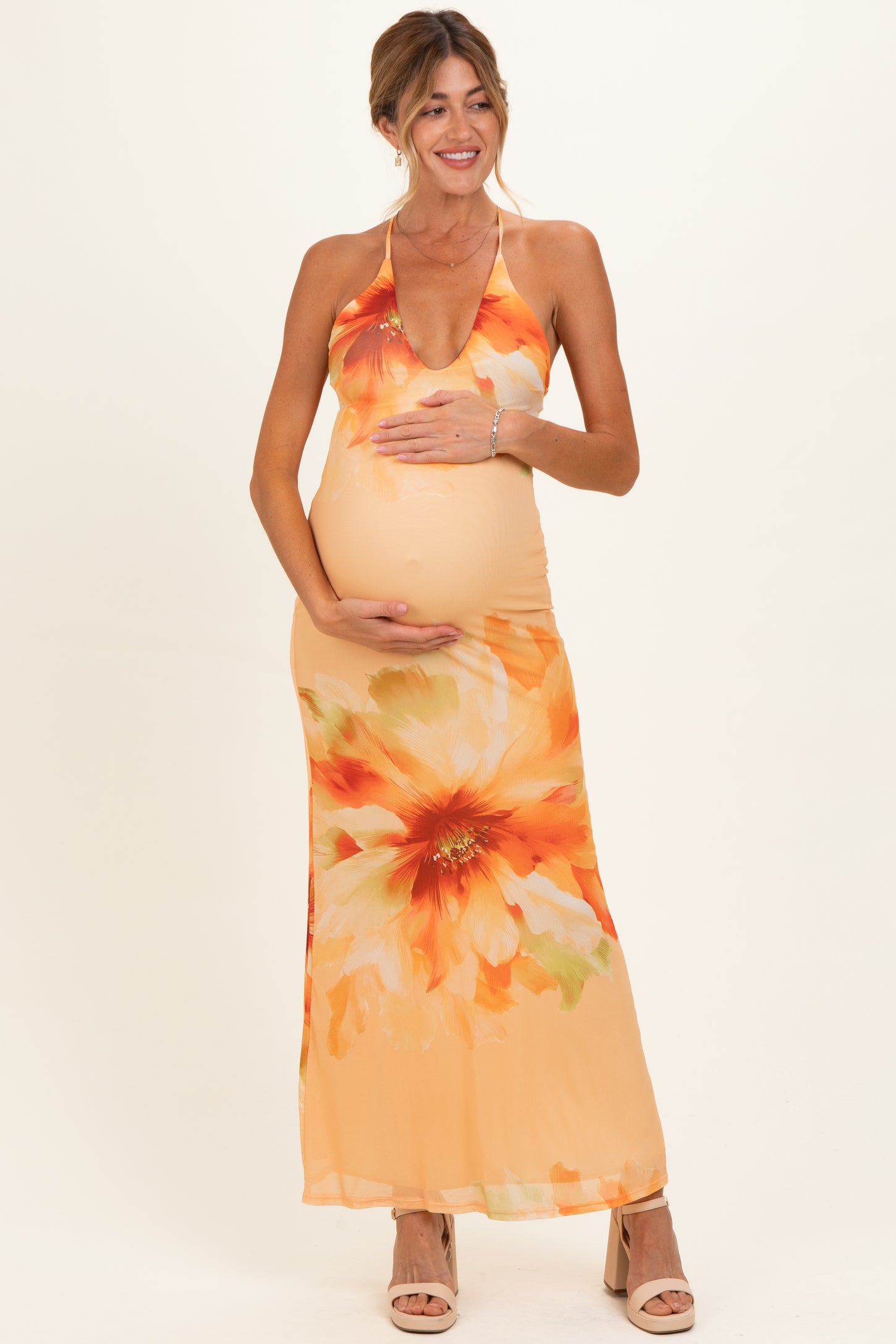 woman wearing a floral maternity maxi dress in orange hues, gently cradling her baby bump