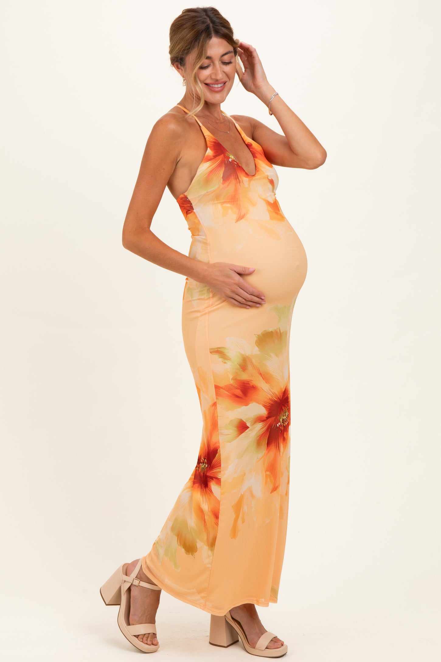woman wearing a floral print maternity dress in orange, with a visible baby bump, standing and smiling