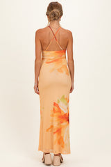 woman wearing a back view of an orange floral maternity maxi dress with a fitted silhouette and crisscross straps
