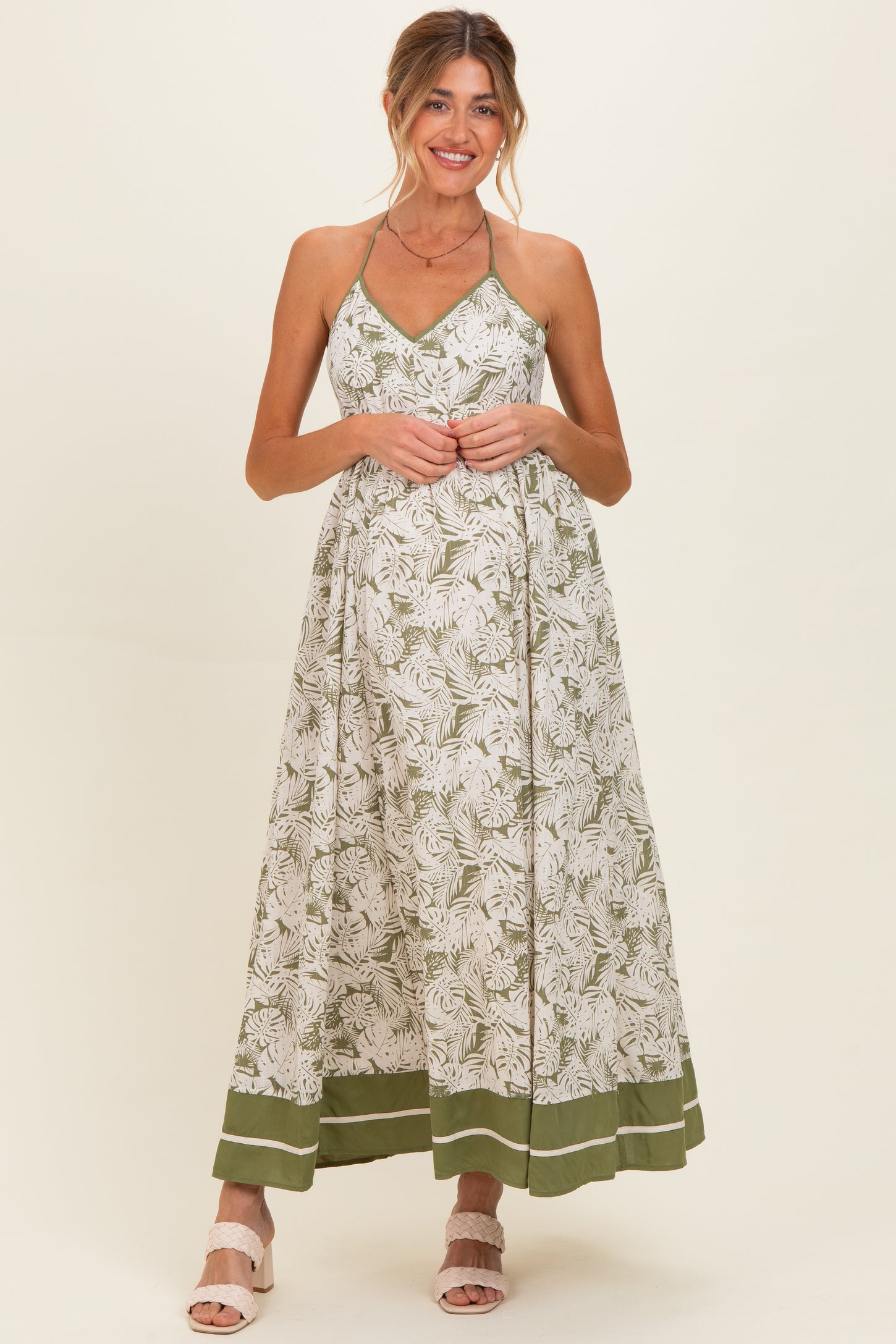 woman wearing a floral green and white maternity maxi dress with a tie halter neckline and a flowing skirt