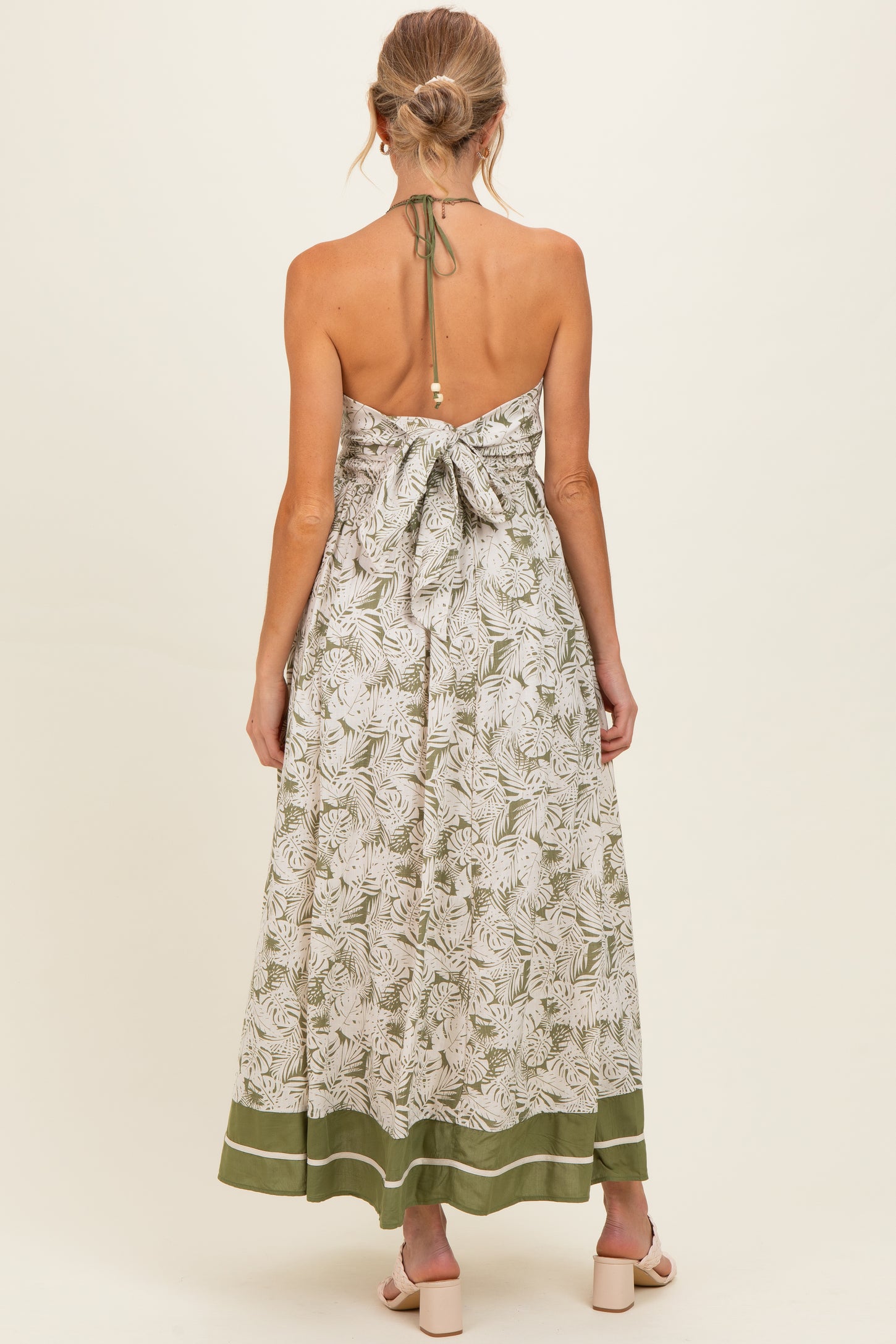 woman wearing a floral print halter maxi dress with a tied back and green trim, showcasing her baby bump