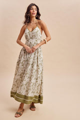 woman wearing a white floral maxi dress with a green hem and halter straps, posing against a neutral background