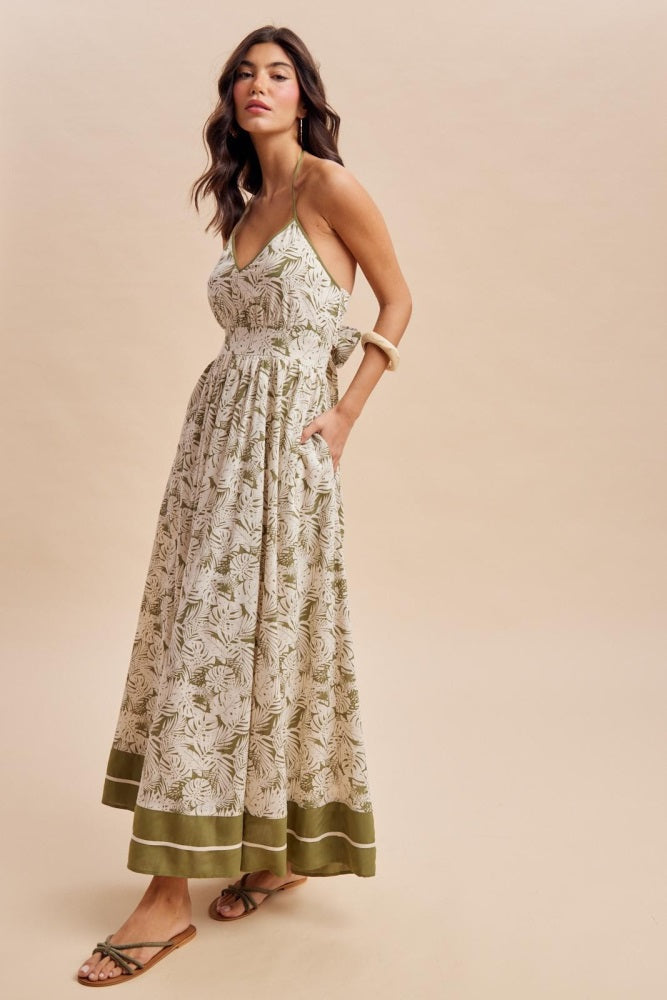 woman wearing a floral print maxi dress with a fitted bodice, waist tie, and pockets, styled with flat sandals