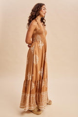 woman wearing a tan maxi dress with white floral patterns and a tiered skirt, standing sideways against a neutral background