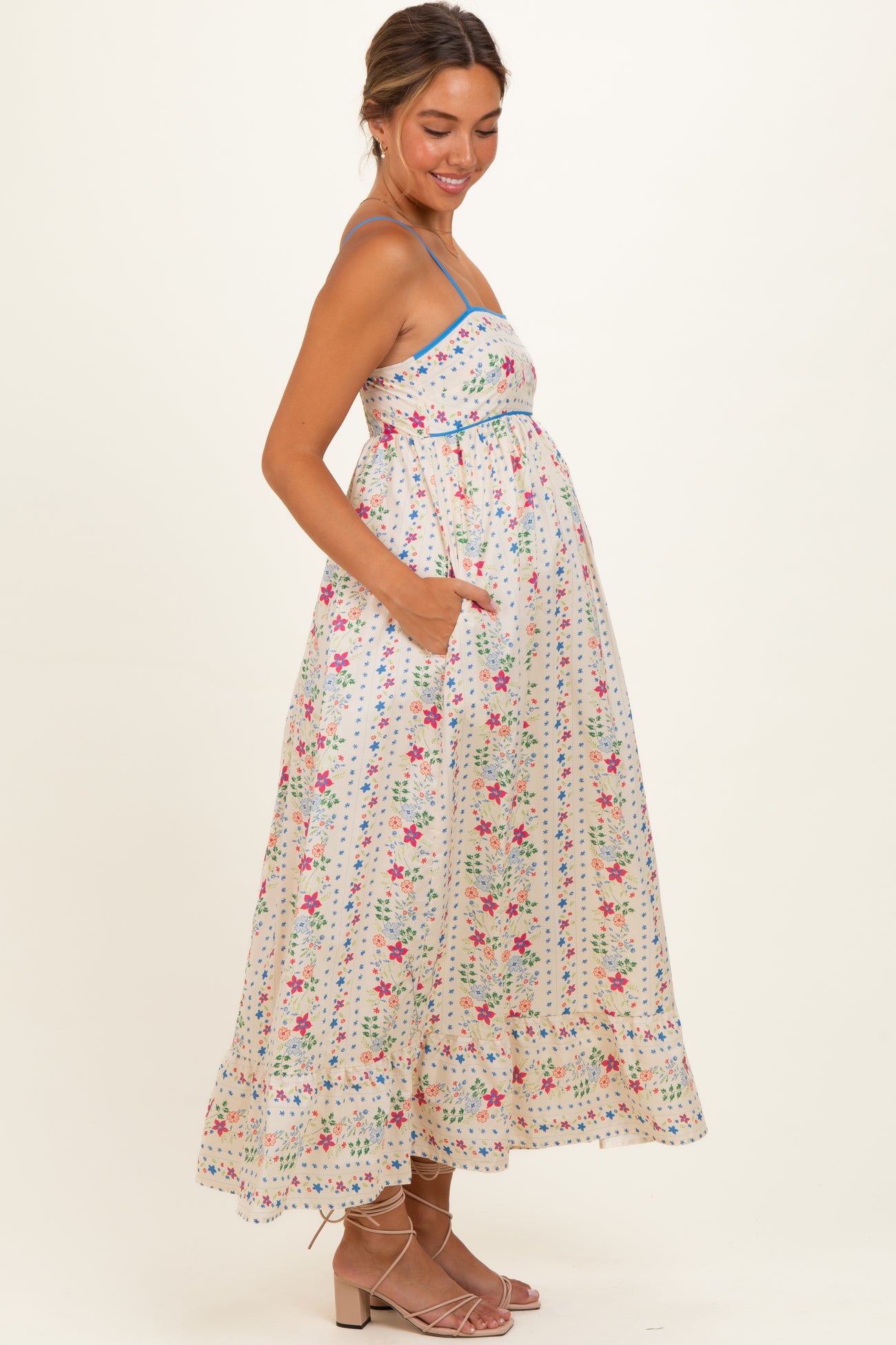 woman wearing a white floral maternity maxi dress with a fitted bodice and pockets, showing her baby bump