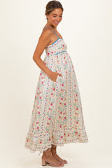 woman wearing a white floral maternity maxi dress with a fitted bodice and pockets, showing her baby bump