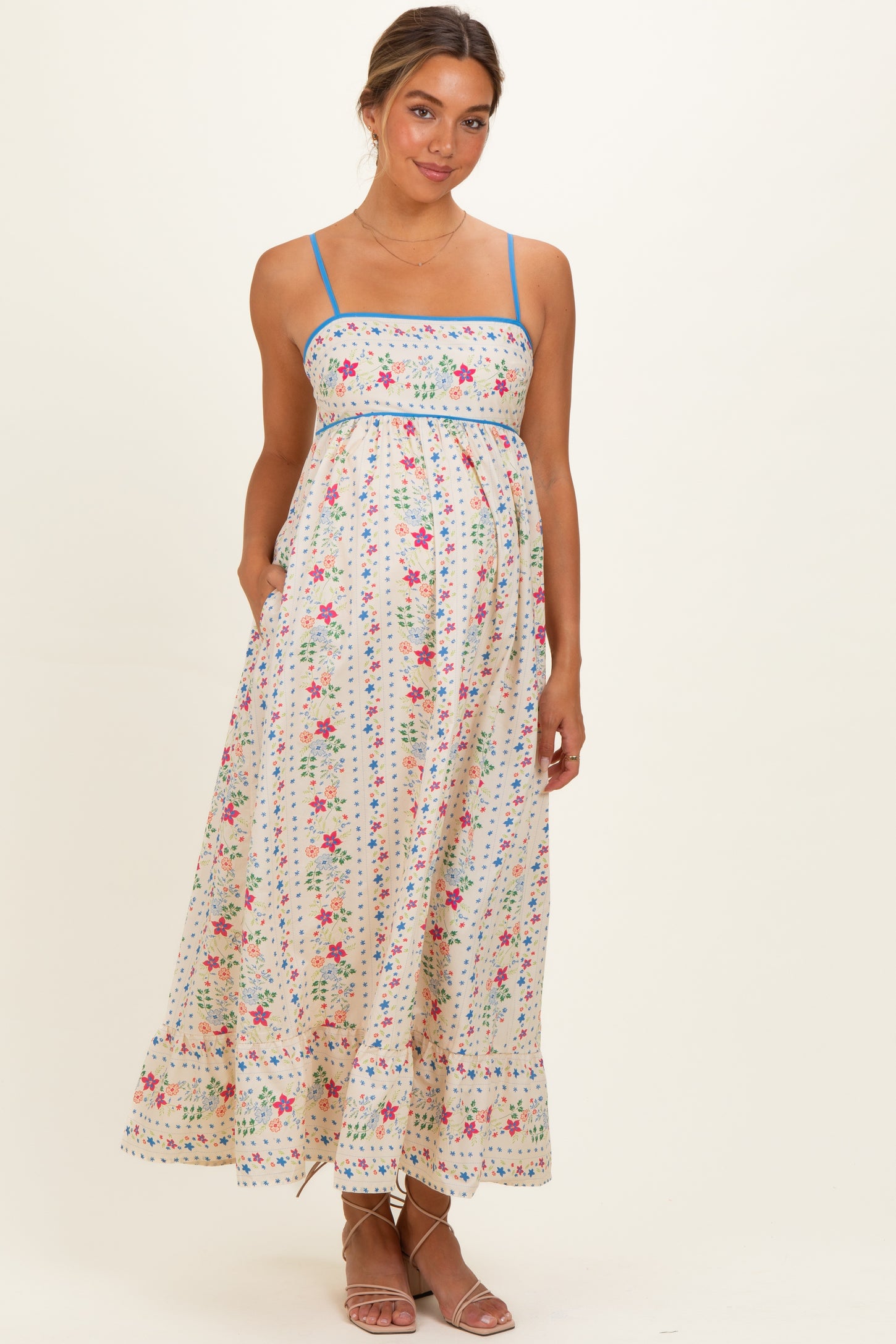 woman wearing a floral print maternity maxi dress with blue straps and pockets, showcasing her baby bump