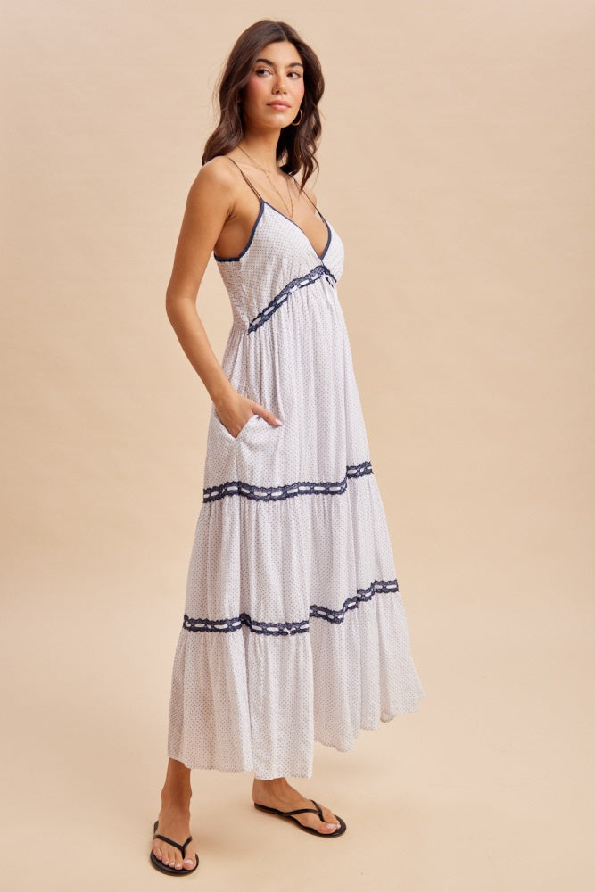 woman wearing a white tiered maxi dress with navy blue accents and pockets, standing on a neutral background