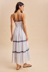 woman wearing a white maxi dress with navy lace details and a smocked back, showing the back view