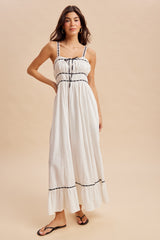 woman wearing a white maxi dress with black trim and spaghetti straps