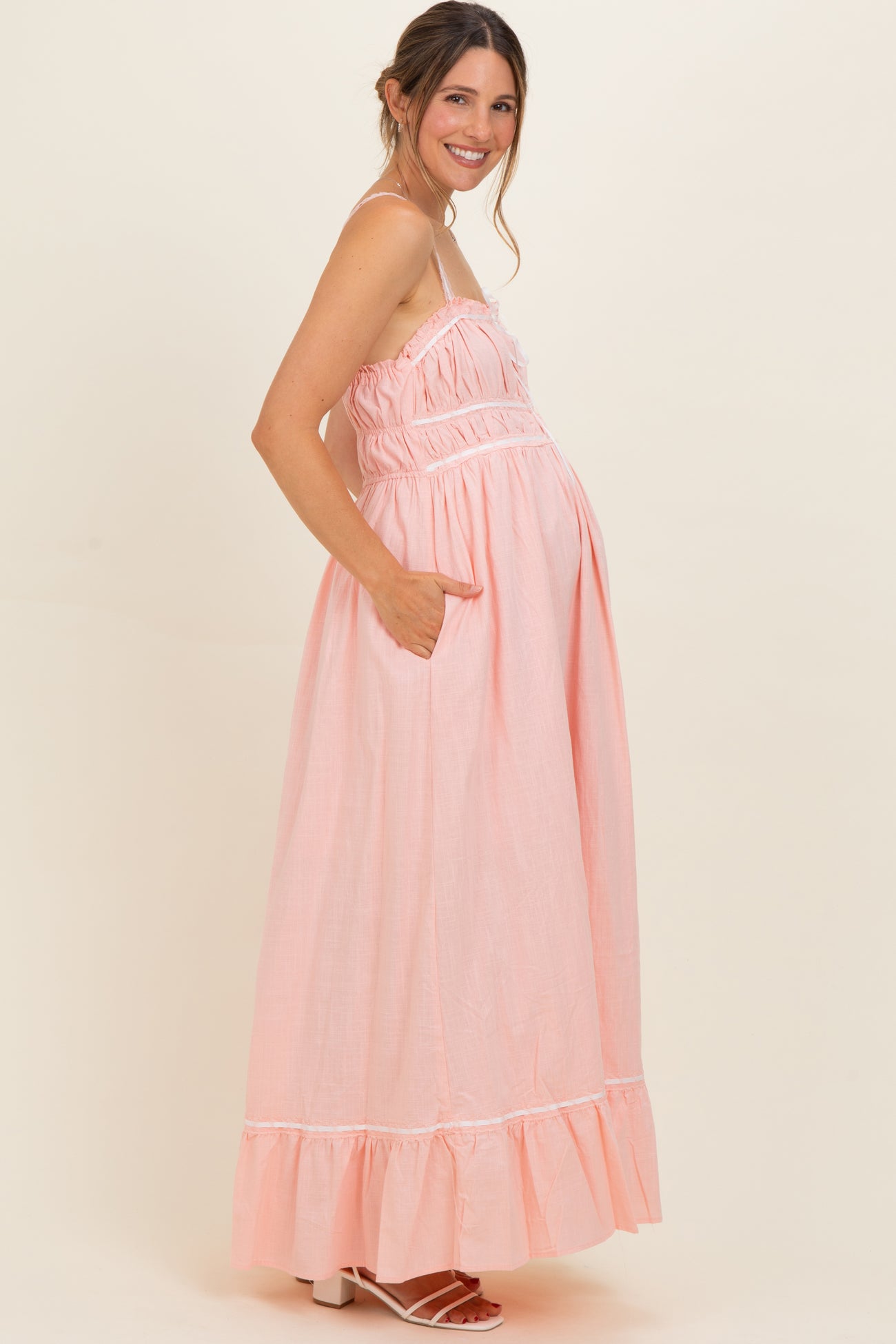 woman wearing a pink maternity maxi dress with adjustable straps and pockets, showcasing her baby bump