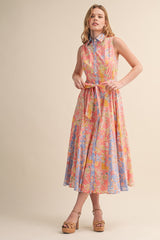woman wearing a sleeveless floral maxi dress with a collared neckline and belted waist in pastel colors