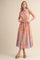 woman wearing a sleeveless floral maxi dress with a collared neckline and belted waist in pastel colors