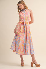 woman wearing a sleeveless pink and blue belted midi dress with a floral pattern and a collar