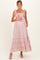 woman wearing a pink floral maternity maxi dress with tie straps and ruffle details, holding her baby bump