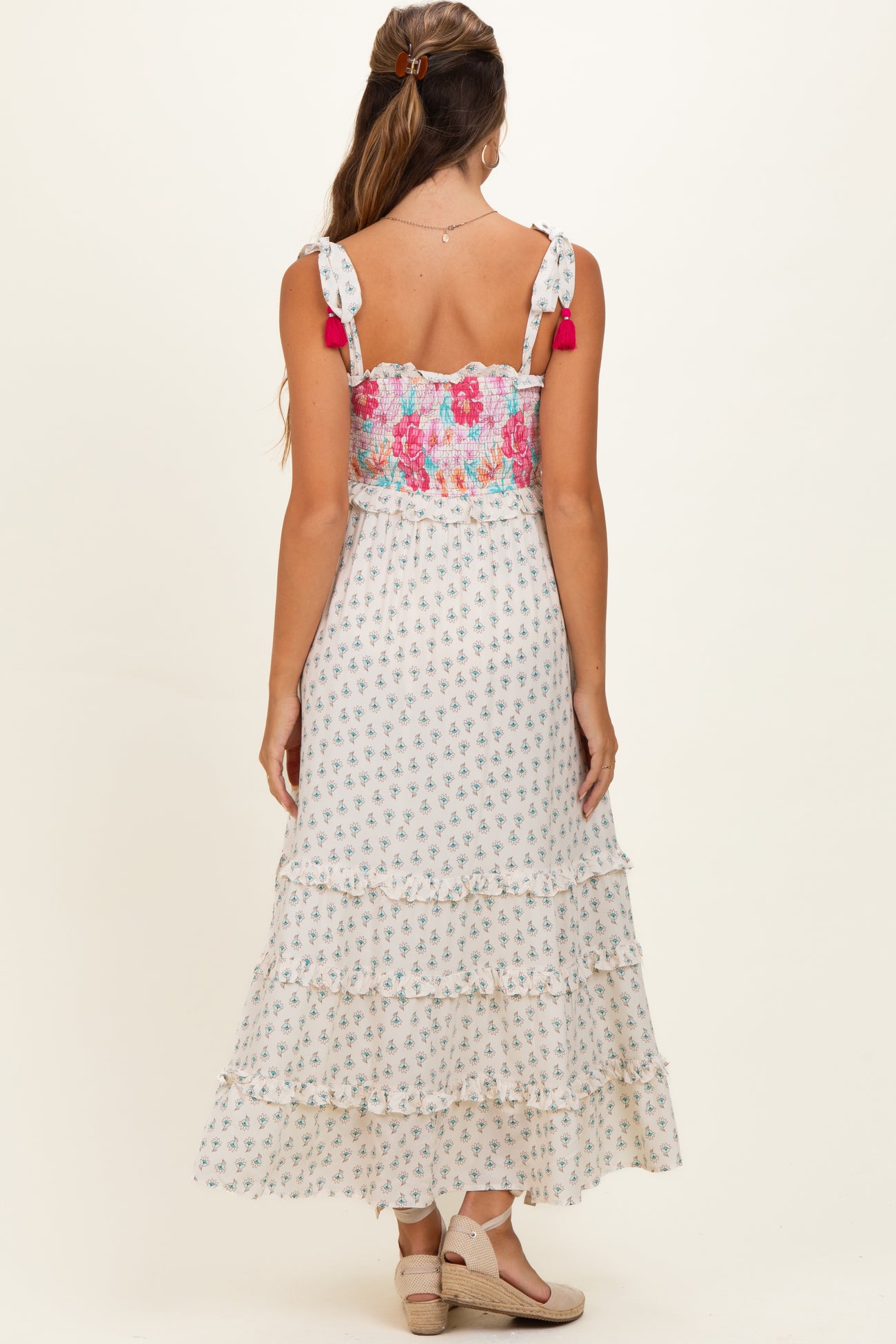 woman wearing a floral tiered maxi dress with adjustable straps and pom pom details, showing her back in maternity wear