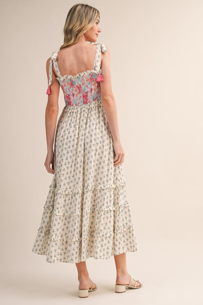 woman wearing a floral patterned maxi dress with tiered skirt and smocked bodice, featuring tie straps and tassels