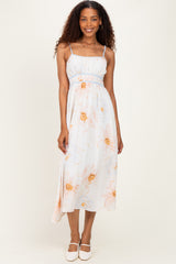 woman wearing a light blue floral maxi dress with thin straps and a fitted bodice, standing with a smile