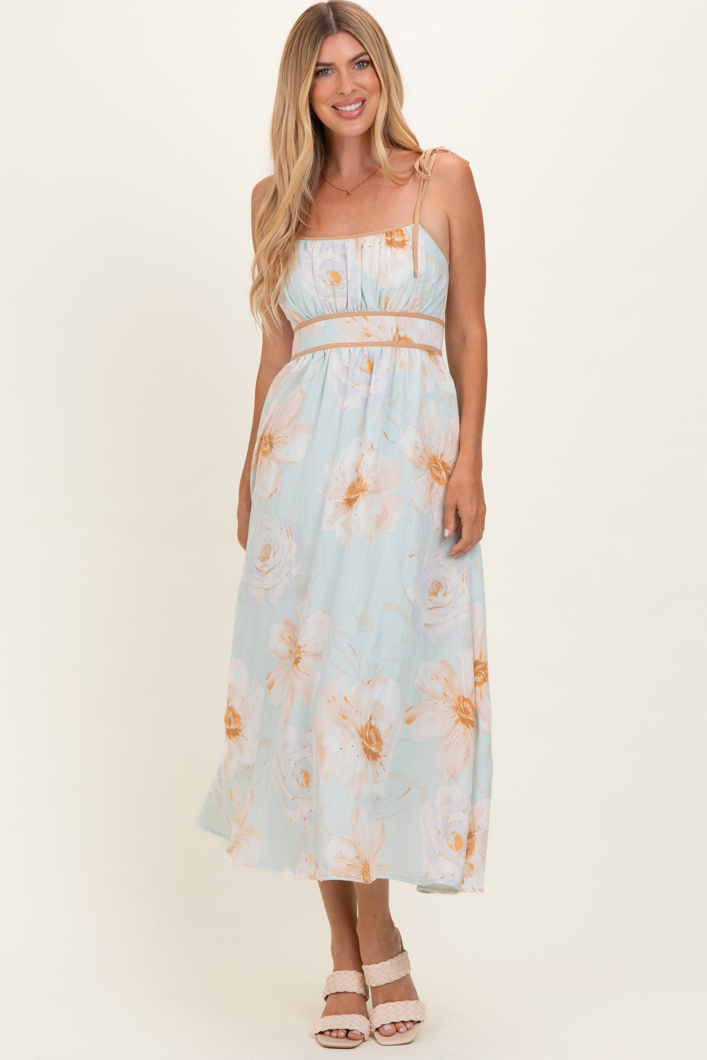woman wearing a light blue floral maxi dress with spaghetti straps and a cinched waist, standing and smiling
