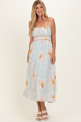 woman wearing a light blue floral maxi dress with spaghetti straps and a cinched waist, standing and smiling
